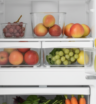 Pessoa organizando morangos, folhas verdes, cenouras e outras frutas e verduras em uma geladeira doméstica limpa e clara.