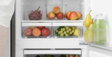 Pessoa organizando morangos, folhas verdes, cenouras e outras frutas e verduras em uma geladeira doméstica limpa e clara.